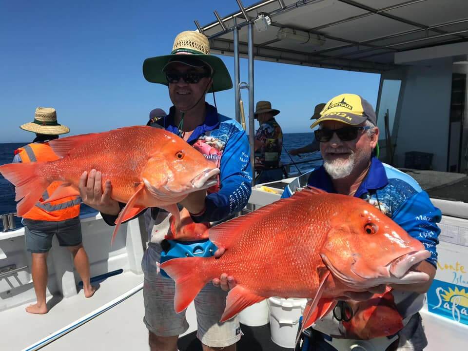 Two men holding pink snapper fish on boat